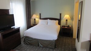 Une chambre d’hôtel avec un lit, deux lampes de chevet, un téléviseur posé sur un meuble en bois et un sol recouvert de moquette.