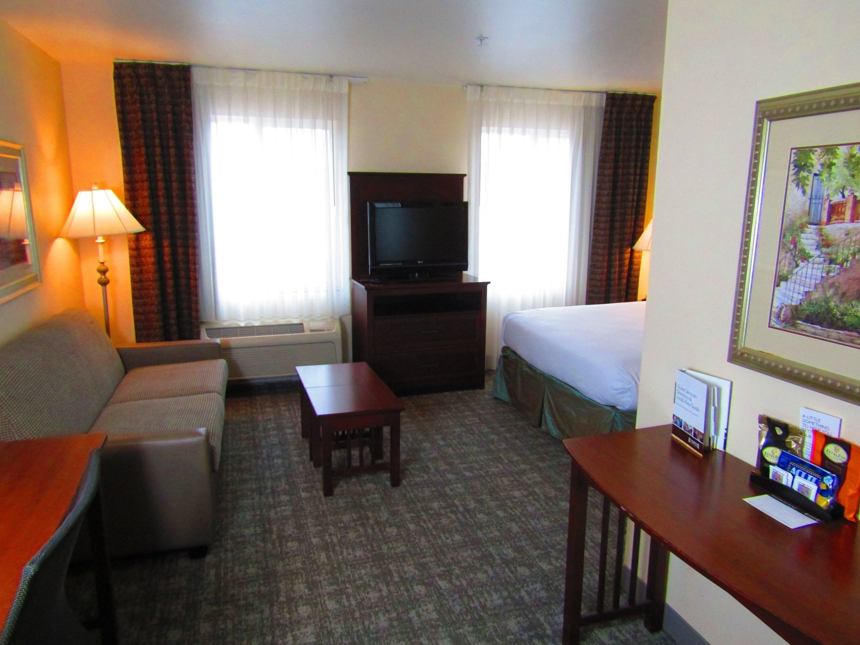 A hotel room with a bed, a desk, a television, a sofa, and a lamp.