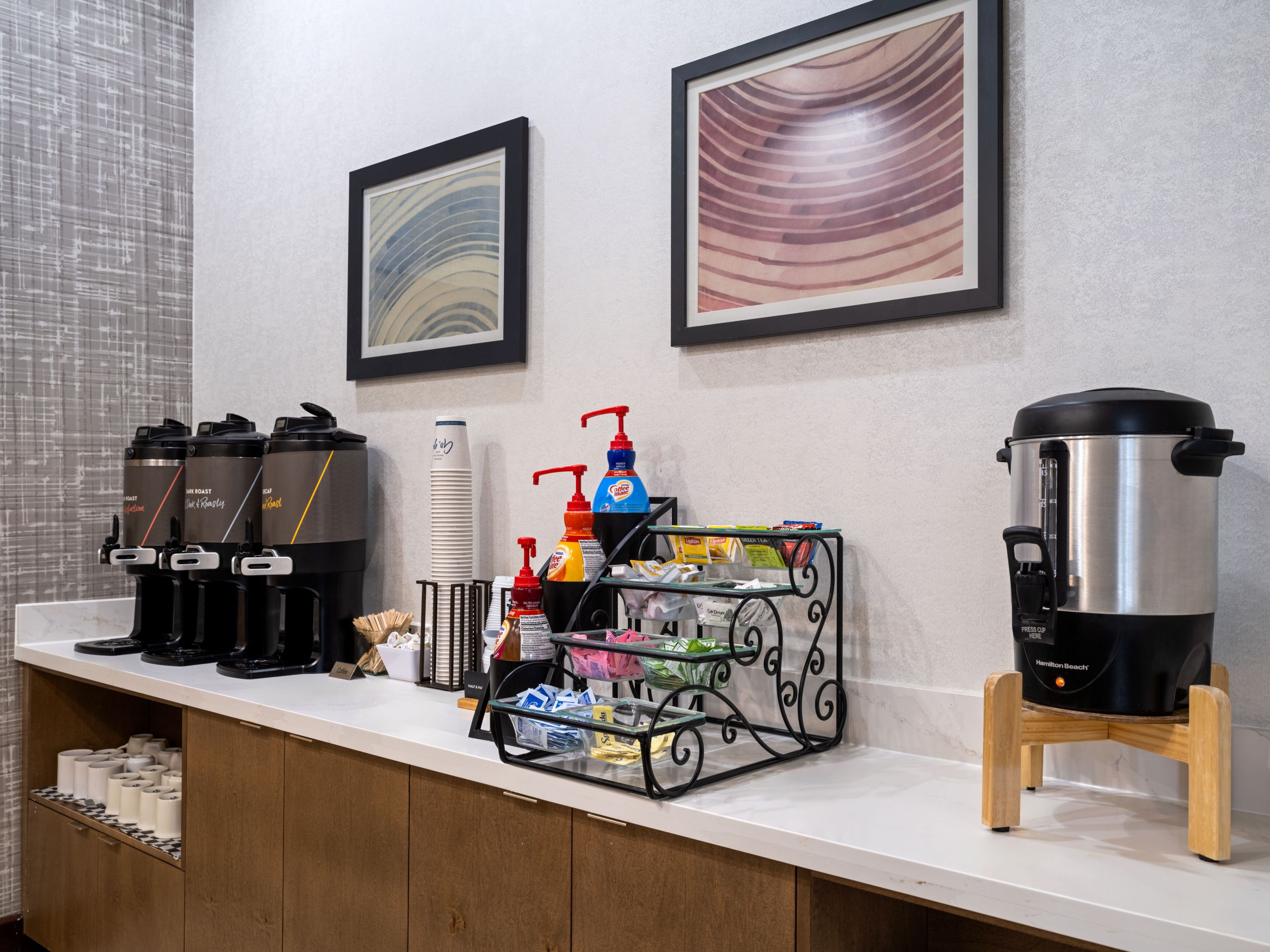 Un buffet de petit-déjeuner d’hôtel avec des machines à café, un distributeur d’eau et une cafetière.