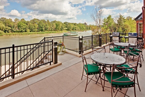 Une terrasse avec des places assises extérieures, une vue sur la rivière et un bateau en arrière-plan.