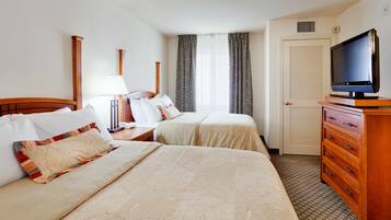 A hotel room with two beds, a television, a dresser, and a window with curtains.