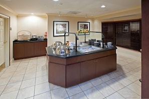 A kitchen area with a central island, a sink, and a countertop with various appliances and utensils. - Studio | Free Breakfast + Outdoor Pool (Plainfield)