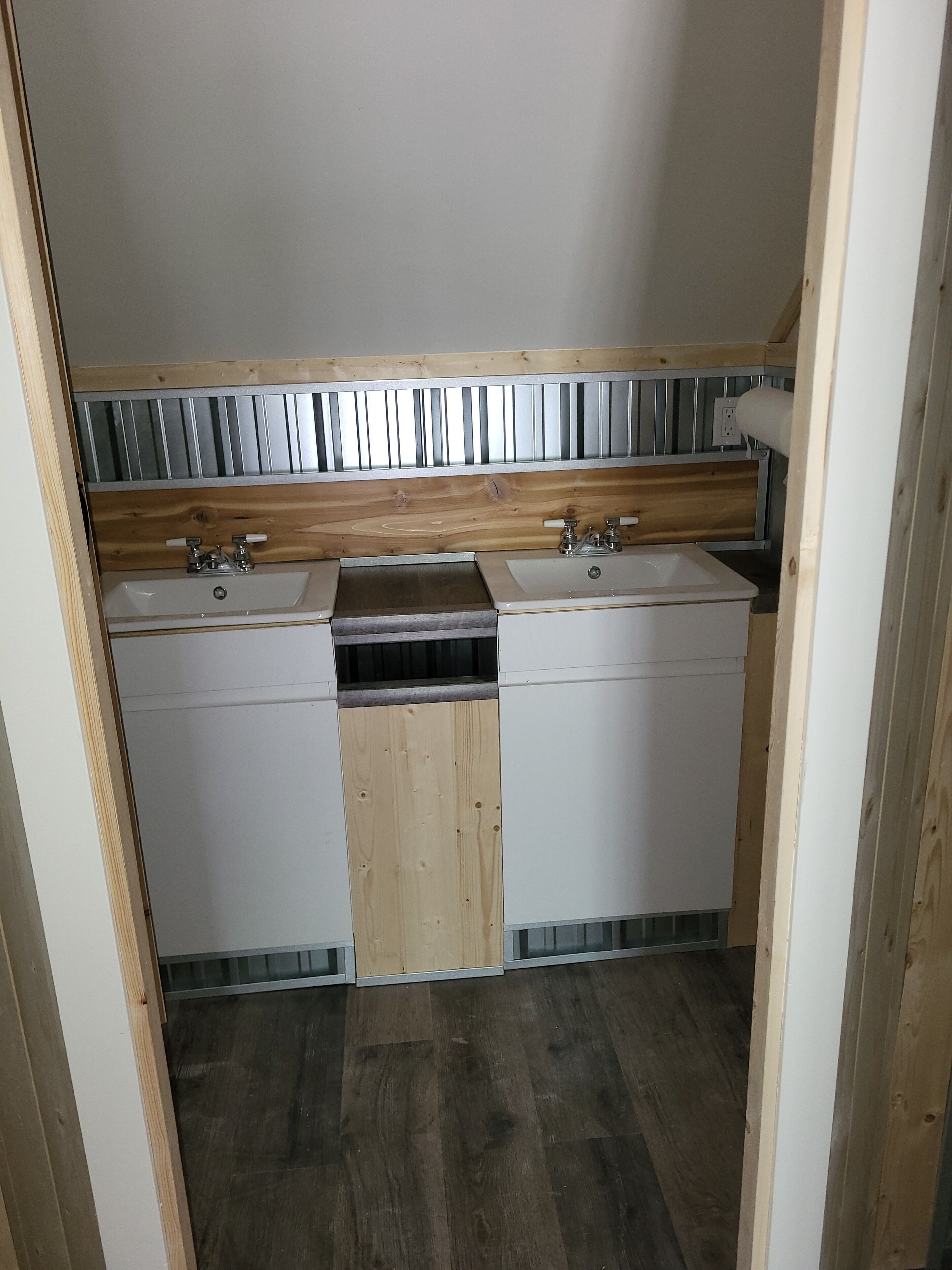 A compact kitchen with two sinks, wooden cabinetry, and a metal backsplash.
