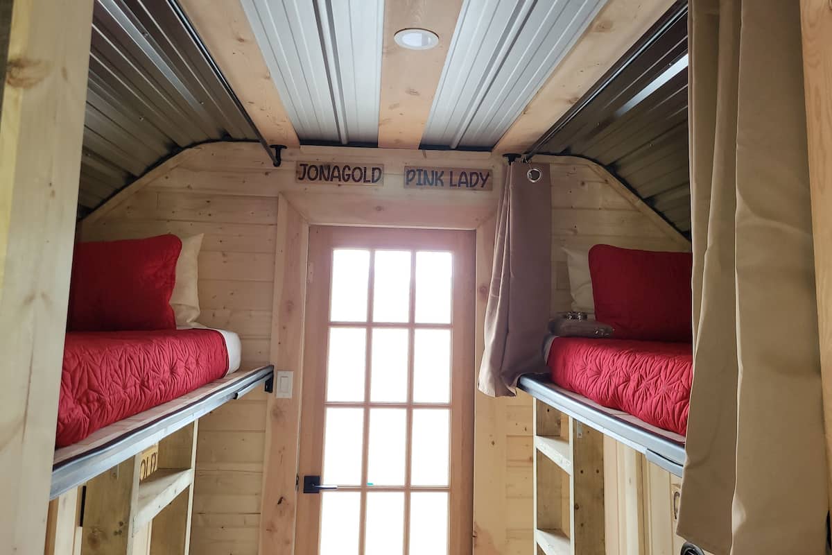 Een gezellige slaapkamer op zolder met twee stapelbedden, elk met een rode matras en hoofdbord. Een houten deur met een raam in het midden zorgt voor natuurlijk licht.