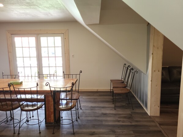 A dining area with a wooden table and metal chairs, a window with blinds, and a staircase leading to a lower level. - The Orchard Hostel Private Bunks (Radium Hot Springs)