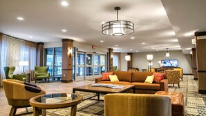 Et hotel lobby med en sofa, lænestole, et sofabord og et fjernsyn.