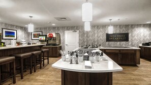 A modern kitchen with a central island, bar stools, a coffee machine, and a sign for free breakfast.