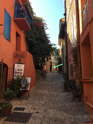 A narrow cobblestone street flanked by buildings with balconies and potted plants.