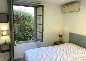 Ein Schlafzimmer mit einem Bett, zwei Nachttischlampen, einem Fenster mit geöffnetem Rollo und einer Klimaanlage an der Wand.