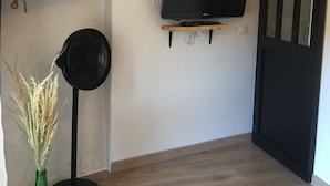 Una stanza con un televisore su un supporto a parete, pavimento in legno, una porta nera e una piccola mensola con oggetti decorativi.