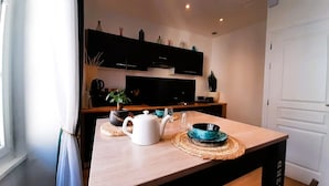 Una cucina moderna con un tavolo in legno, un bollitore bianco, una ciotola blu e una pianta in vaso.