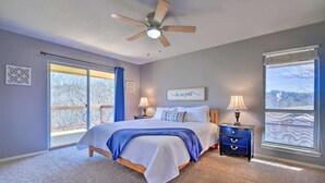Un dormitorio con cama, dos mesitas de noche, ventilador de techo y un ventanal grande.