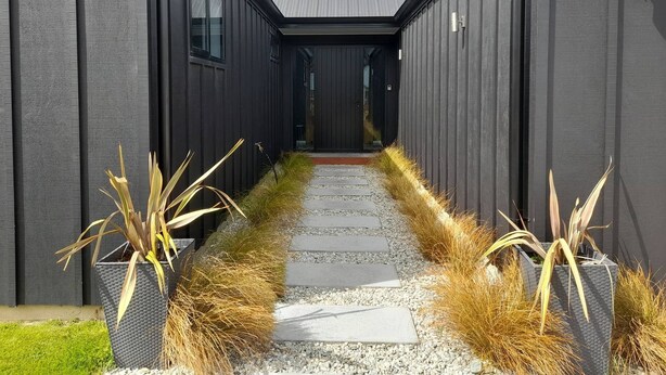 A modern building with a narrow pathway leading to a dark entrance.