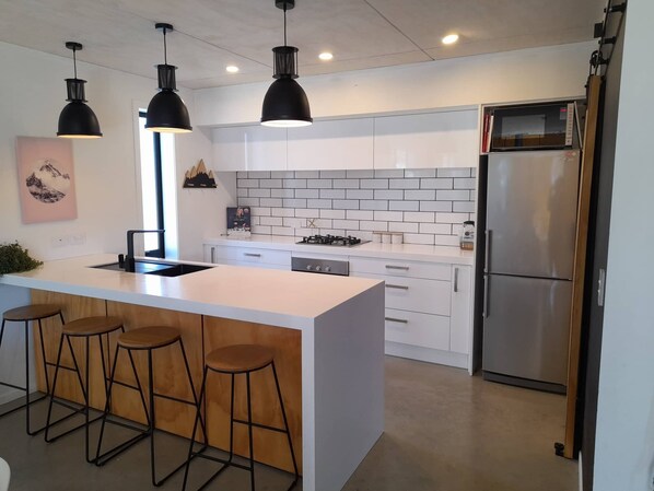A modern kitchen with a central island, bar stools, pendant lighting, and a stainless steel refrigerator.
