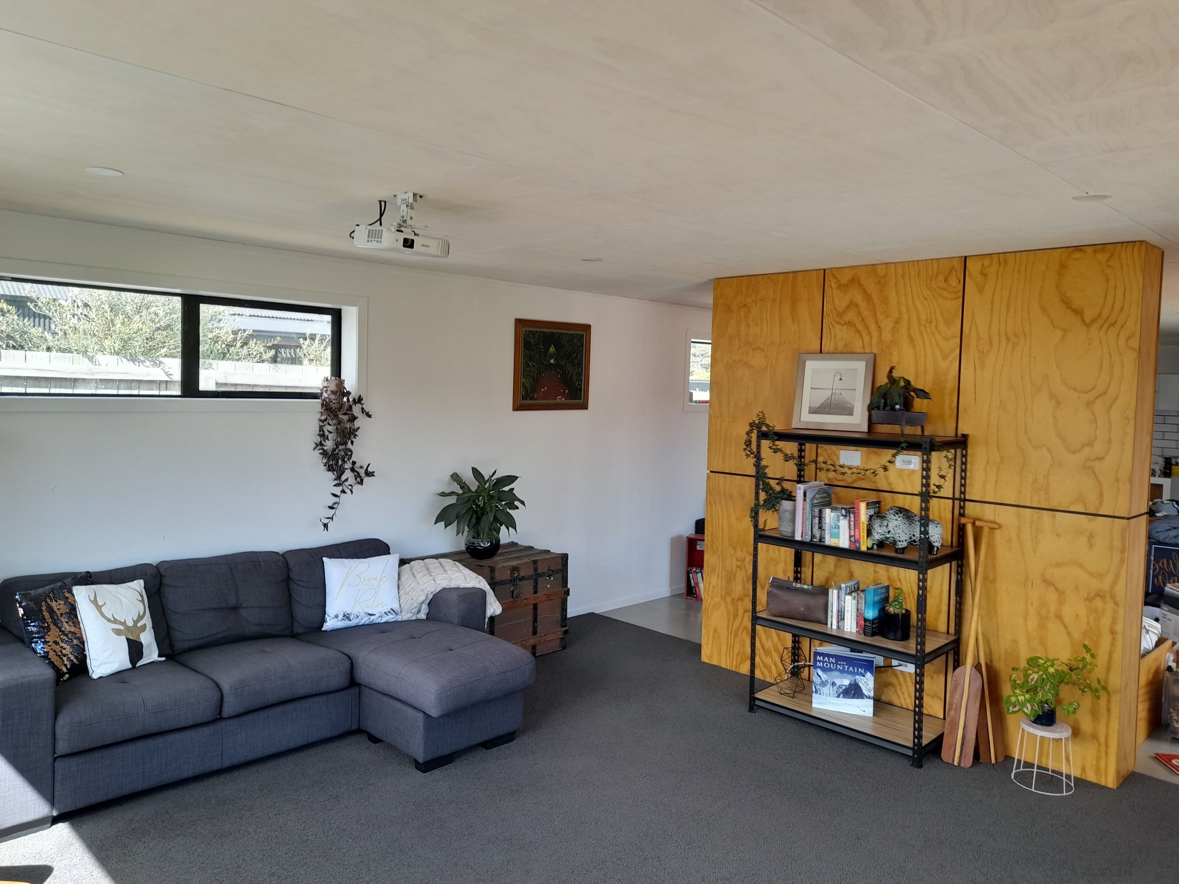 A modern living room with a grey sectional sofa, a wooden bookshelf, and a ceiling projector.
