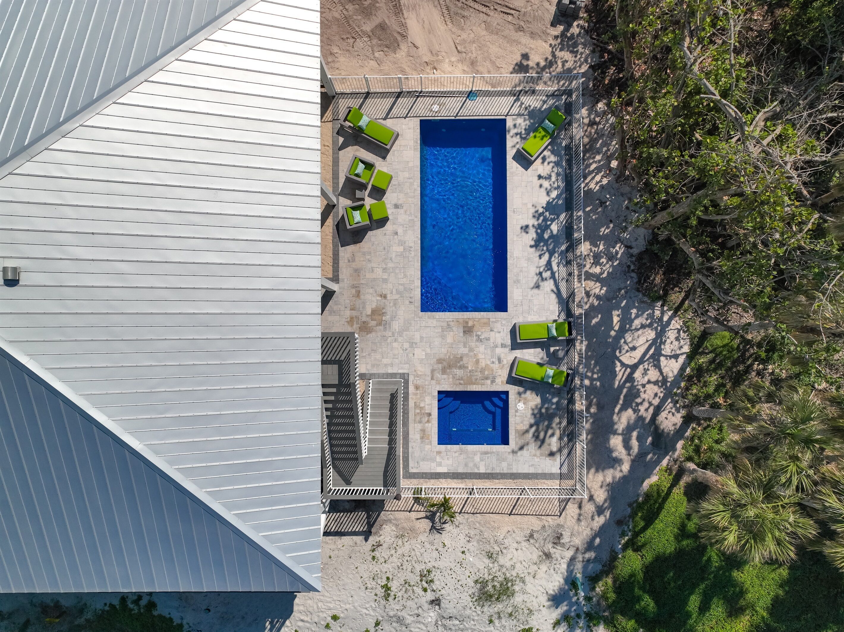 Vue aérienne d’un espace piscine comprenant deux piscines, entourées de chaises longues et d’une terrasse.