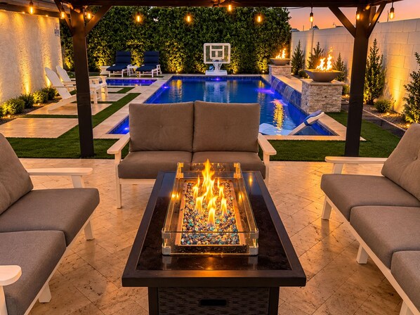 An outdoor patio with a fire feature, seating, and a pool.