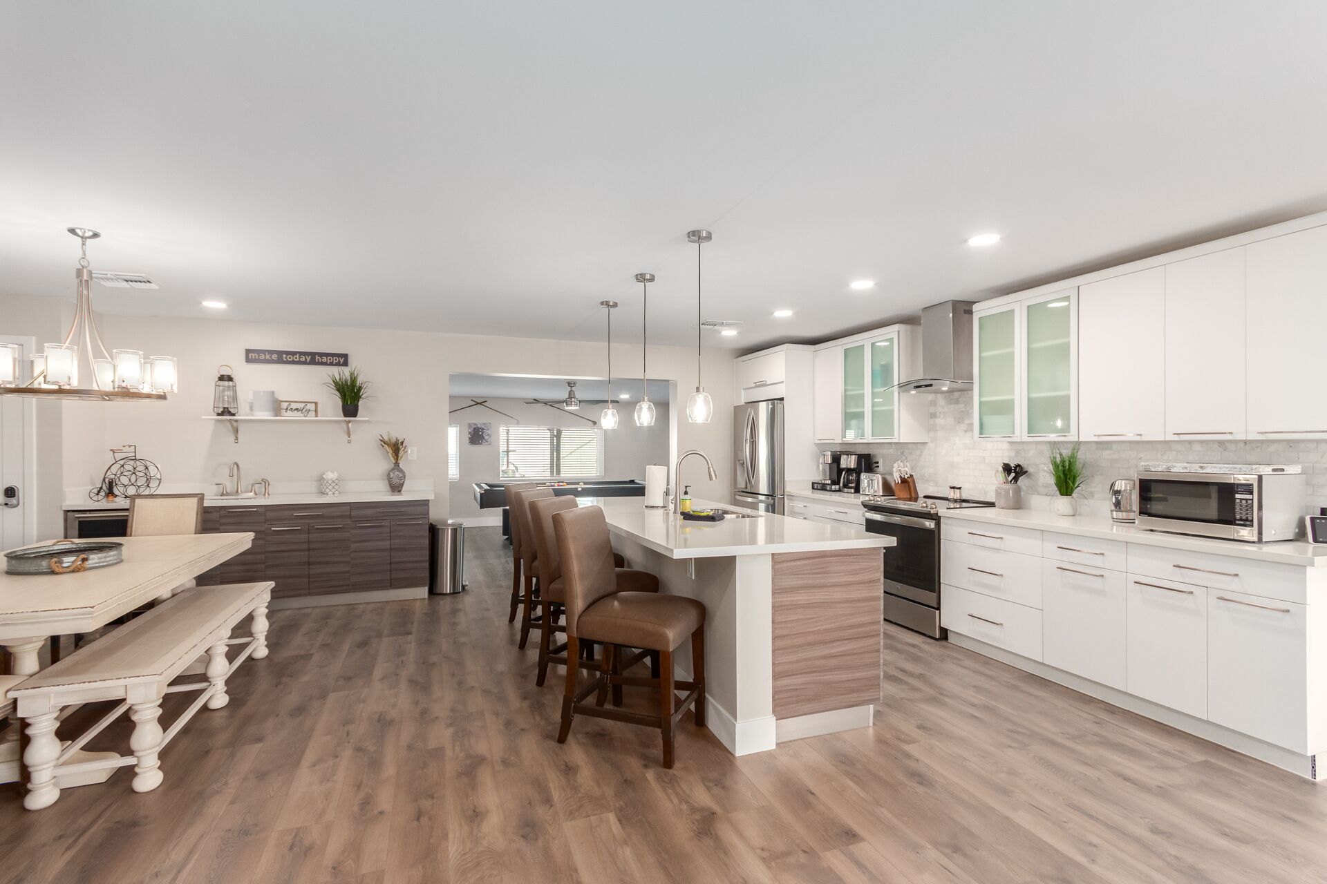 A modern kitchen with white cabinets, a central island, and a dining area with a wooden table and benches.