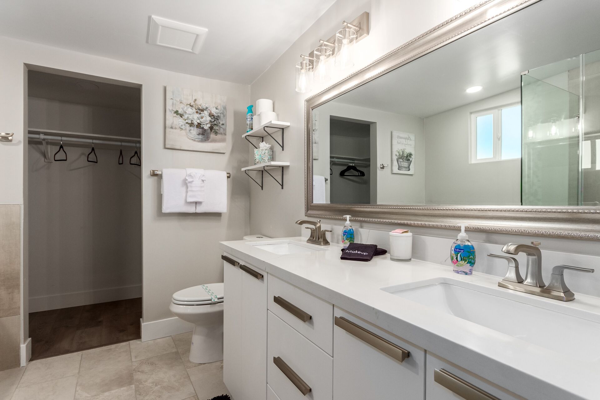 Een moderne badkamer met een grote spiegel, twee wastafels en een toilet. Er liggen handdoeken en toiletartikelen op het aanrecht.