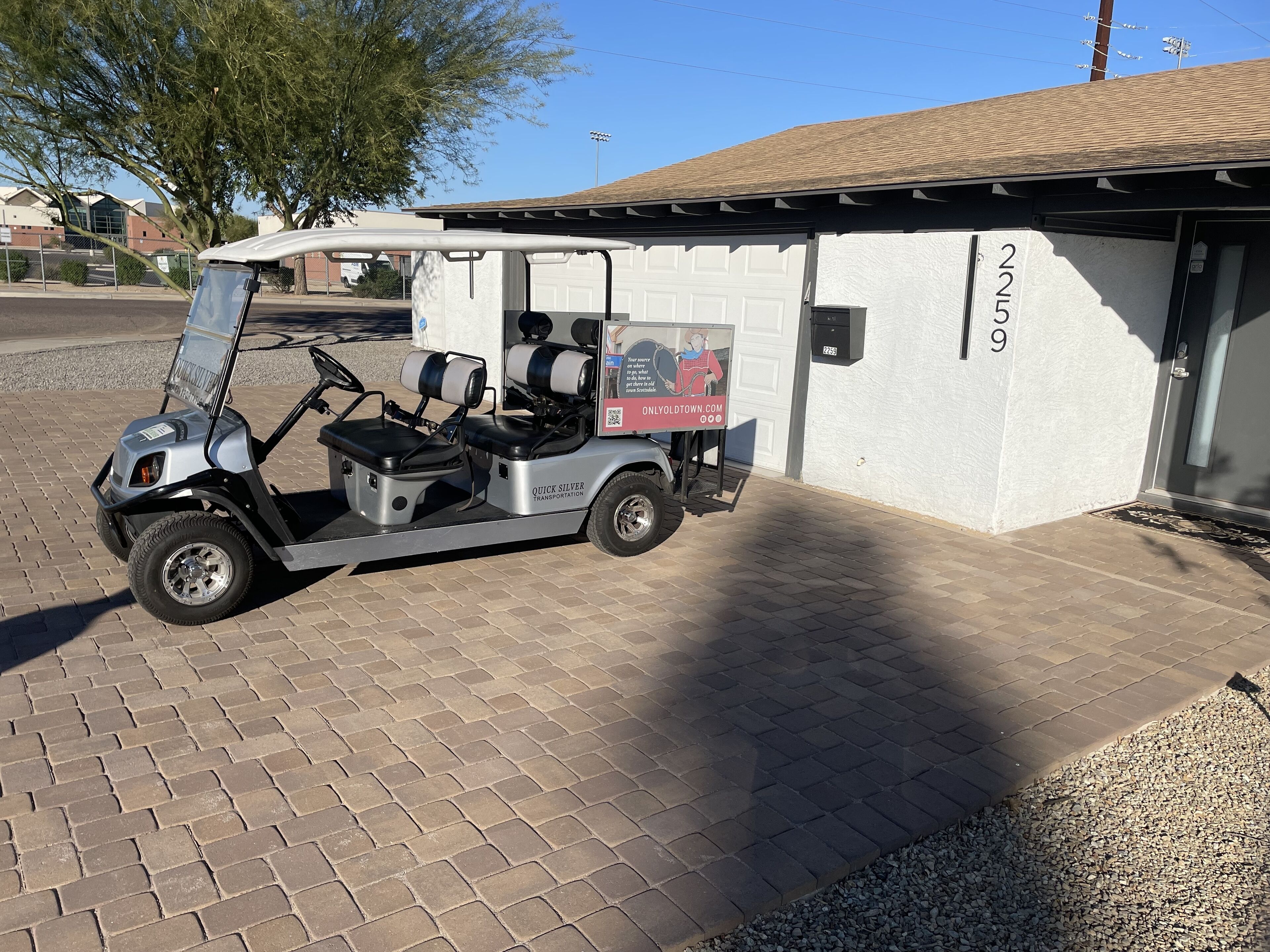 A golf cart parked in front of a building with a garage door, number 2259, and a small sign advertising a website.