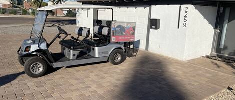 A golf cart parked in front of a building with a garage door, number 2259, and a small sign advertising a website.