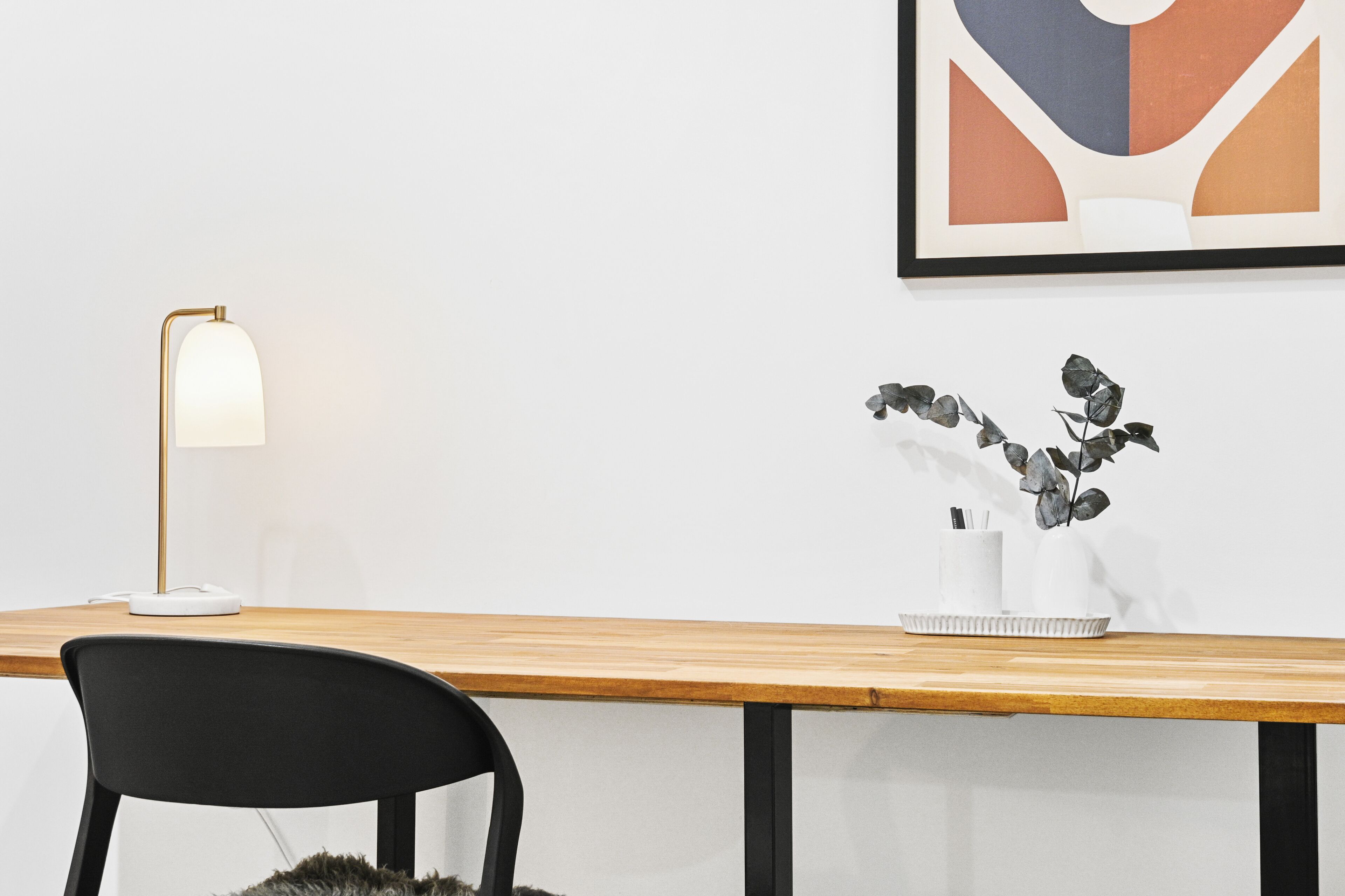 Un bureau moderne avec une lampe, une chaise et un vase contenant une plante.