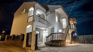 Una casa a due piani con un balcone al secondo piano, un muro in pietra e un ingresso con cancello.