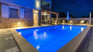 Una piscina con facciata in pietra e zona relax coperta con sedie e ombrelloni.