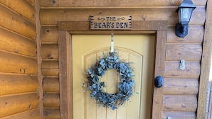 Una puerta de madera con un adorno de guirnalda y un cartel que dice "The Bear's Den".