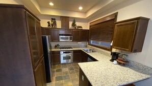 Una cocina con armarios de madera oscura, encimera de granito, refrigerador de acero inoxidable, microondas, horno y pileta.