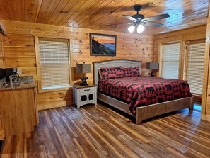 A wooden cabin bedroom with a bed, nightstands, a ceiling fan, and a painting on the wall.