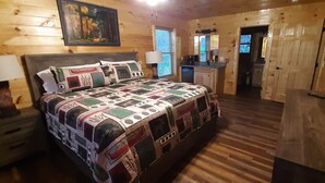 A wooden cabin bedroom with a quilted bedspread, a nightstand with a lamp, a wooden headboard, and a painting on the wall. - Mountain Porches at Blackberry Ridge  (Near everything) (Pigeon Forge)