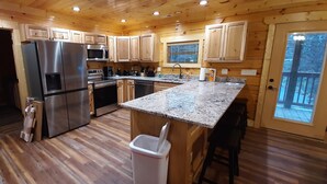 A modern kitchen with wooden cabinetry, stainless steel appliances, a granite countertop, and a view of the outdoors. - Mountain Porches at Blackberry Ridge  (Near everything) (Pigeon Forge)