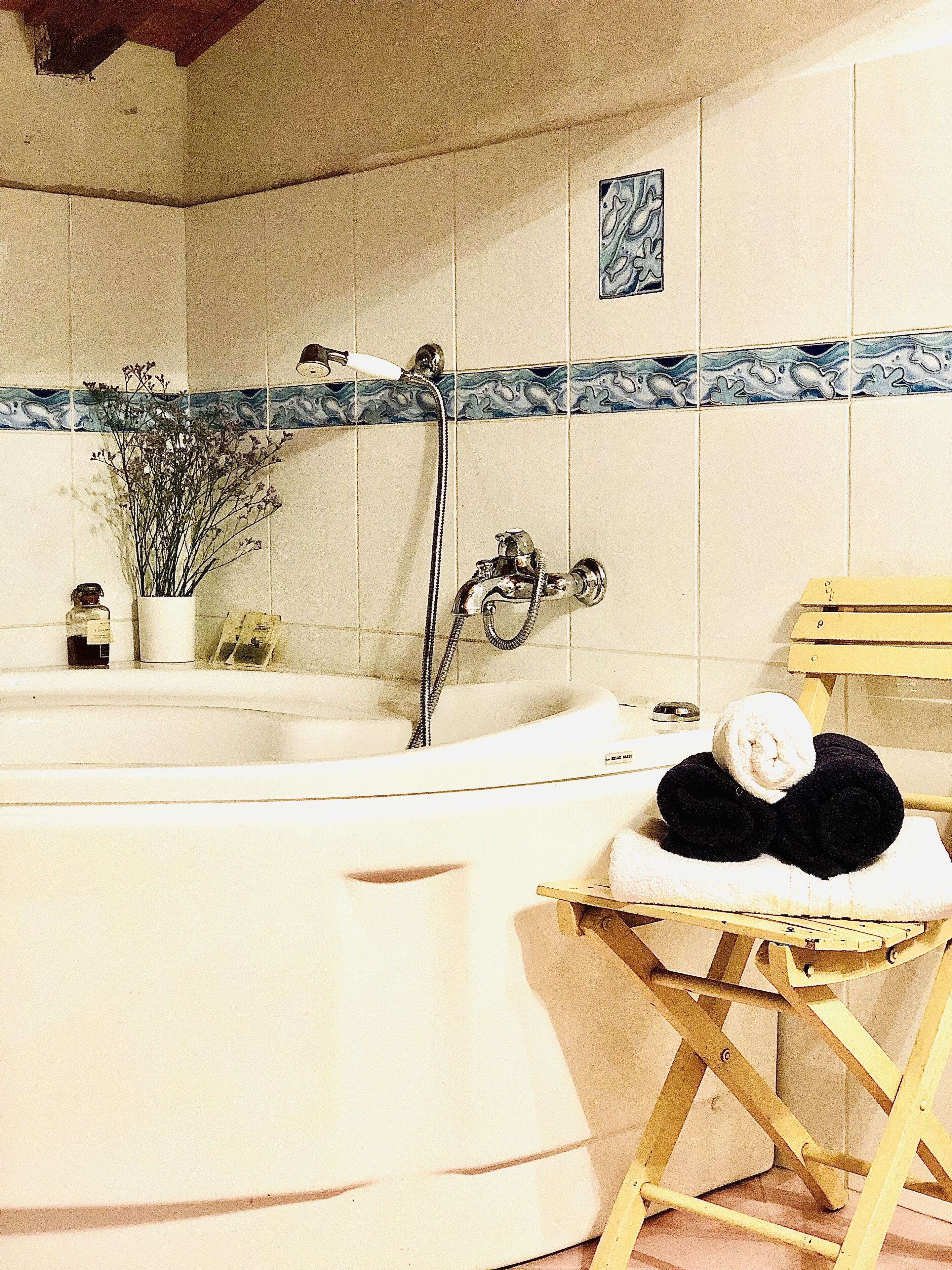 Een badkamer met een bad, een douche en een houten kruk met handdoeken.