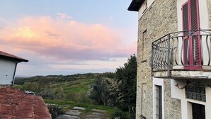Un edificio de piedra con balcón y contraventanas rosas, con vistas a un paisaje montañoso.