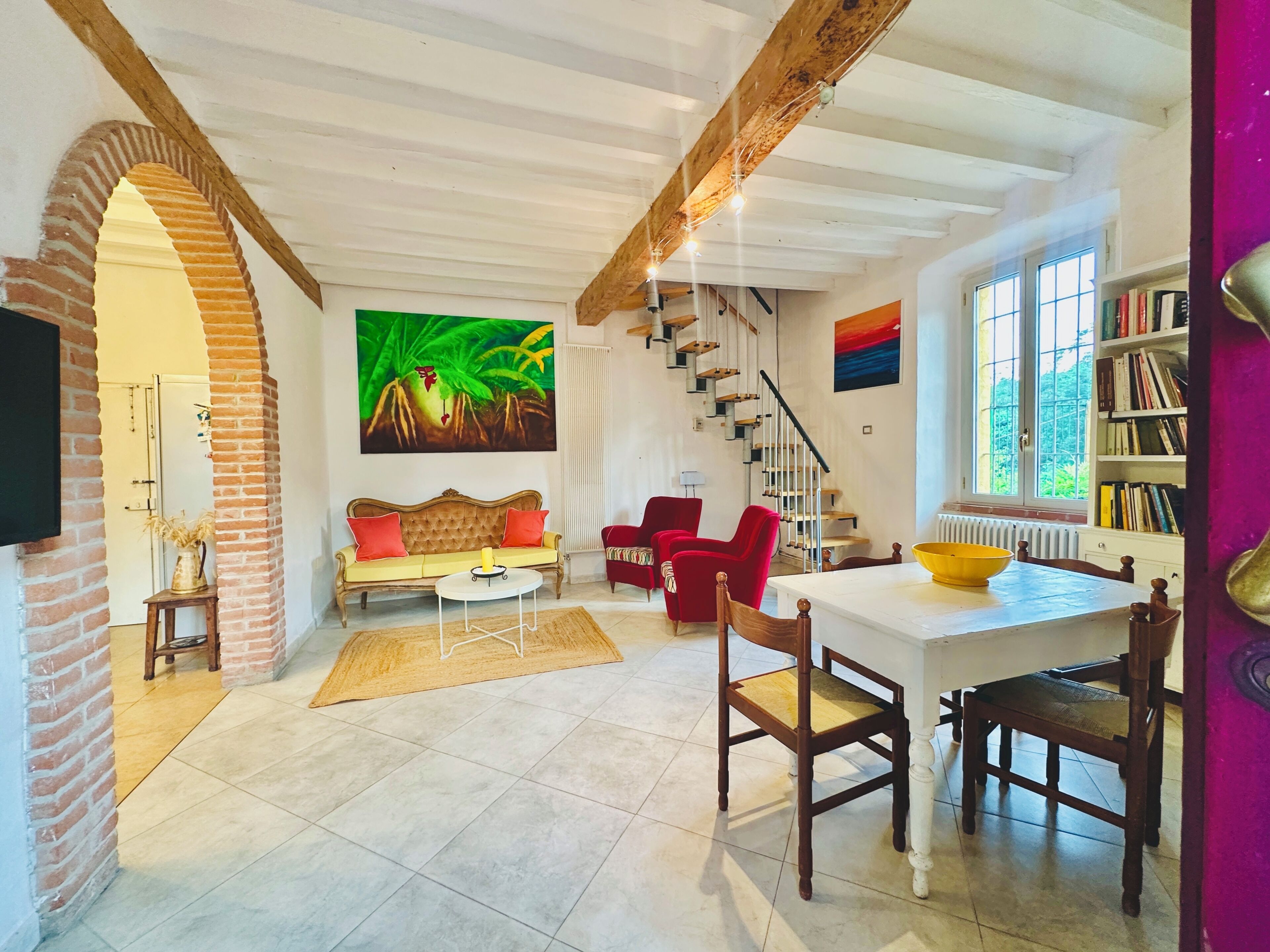 A spacious living area with a sofa, chairs, a dining table, and a staircase.