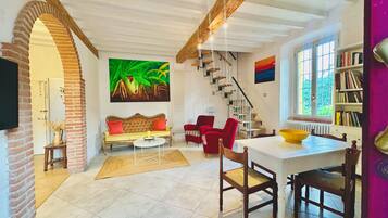 A spacious living area with a sofa, chairs, a dining table, and a staircase.