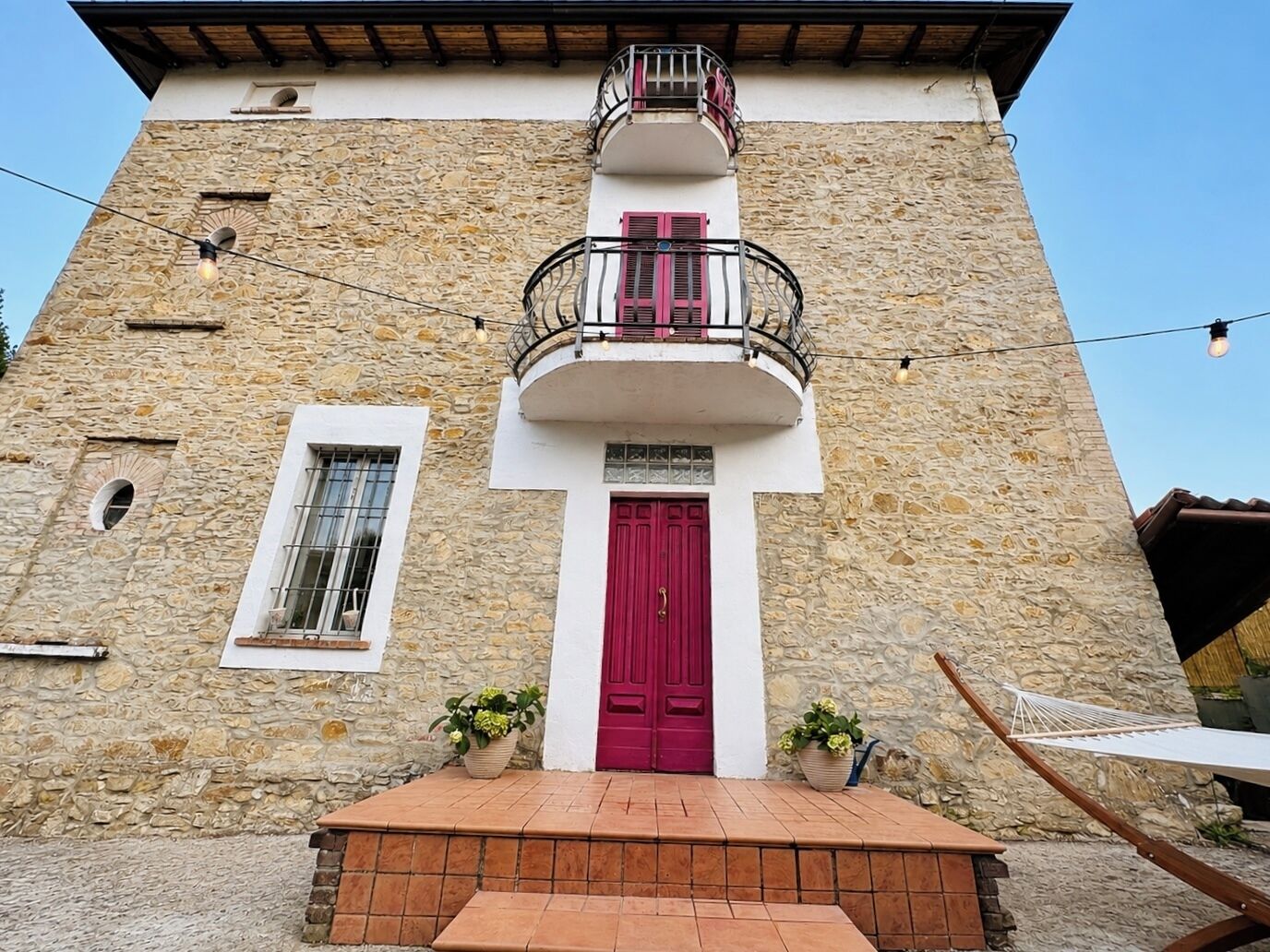 A two-story building with a stone facade, a red door, and a balcony with a wrought iron railing.
