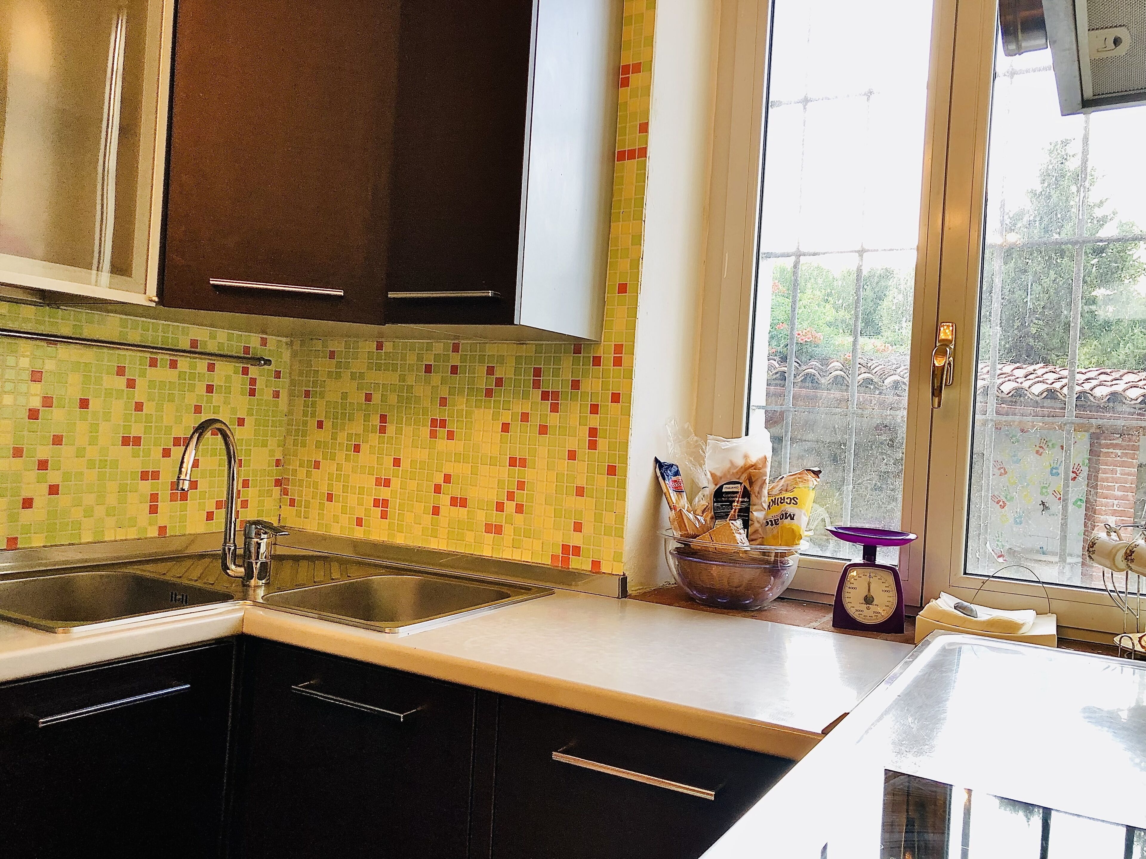 Una cucina con un lavello doppio, una finestra vista verde e un orologio decorativo.