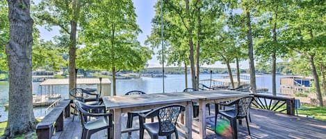 Una terraza de madera con una mesa y sillas que da a un lago, rodeada de árboles.