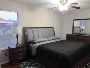 Un dormitorio con cama, mesita de noche, lámpara, cómoda, espejo y ventilador de techo.