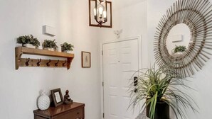 Un couloir avec un porte-manteau en bois, une petite table sur laquelle se trouve une statue, une plante en pot et un miroir fixé au mur.