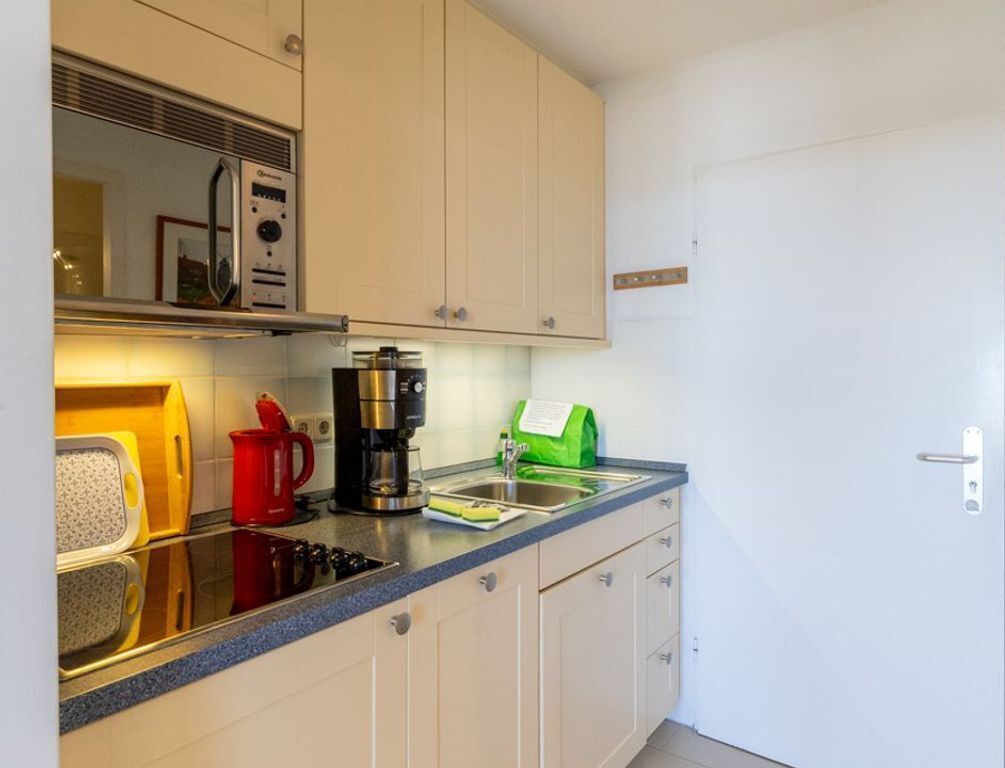 A compact kitchen with a microwave, coffee maker, and a green bag on the counter.