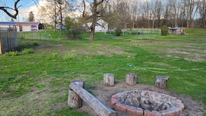 A fenced outdoor area with a fire pit, wooden stumps, and a grassy field. - Charming home with a pool (Michigan City)