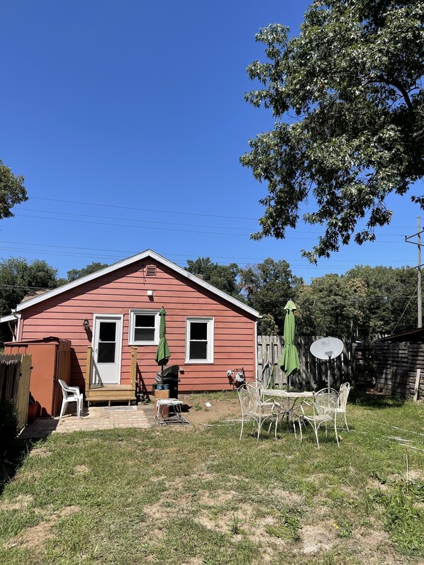 Une maison rouge avec un porche à l’avant, une table de patio et un parasol vert.
