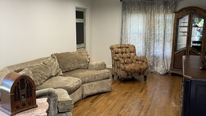 A living room with a sectional sofa, a tufted armchair, a wooden coffee table, and a vintage radio. - Charming home with a pool (Michigan City)
