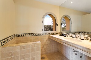 A bathroom with a beige tiled wall, a sink with a mirror, and a window with an arched top.