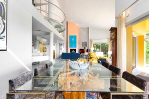Una sala de estar moderna con una mesa de comedor de vidrio, un sofá azul y una escalera que conduce a un nivel superior.