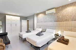 A hotel room with two beds, a sofa, a wardrobe, and an air conditioning unit.