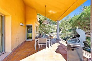 Eine Terrasse im Freien mit Esstisch und Stühlen, einem Grill und einem gelben Sonnenschirm.